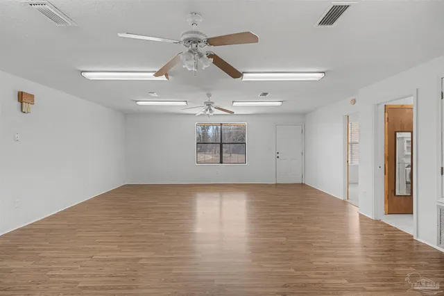 a view of an empty room with wooden floor ceiling fan