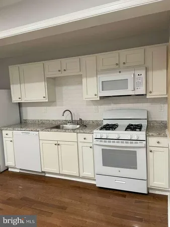 a white kitchen with granite countertop a stove top oven a sink and dishwasher