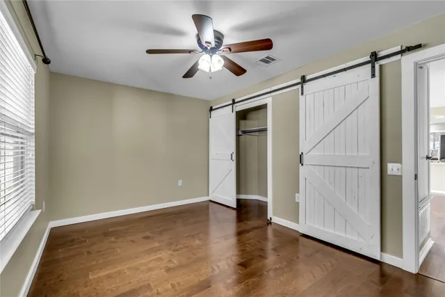 an empty room with wooden floor fan and windows