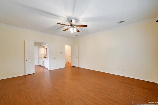a view of an empty room with wooden floor and a ceiling fan