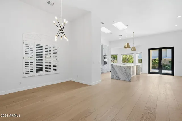 a view of an empty room with wooden floor kitchen view and a window