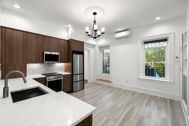 a kitchen with stainless steel appliances a stove top oven a sink dishwasher a refrigerator and a dining table with wooden floor