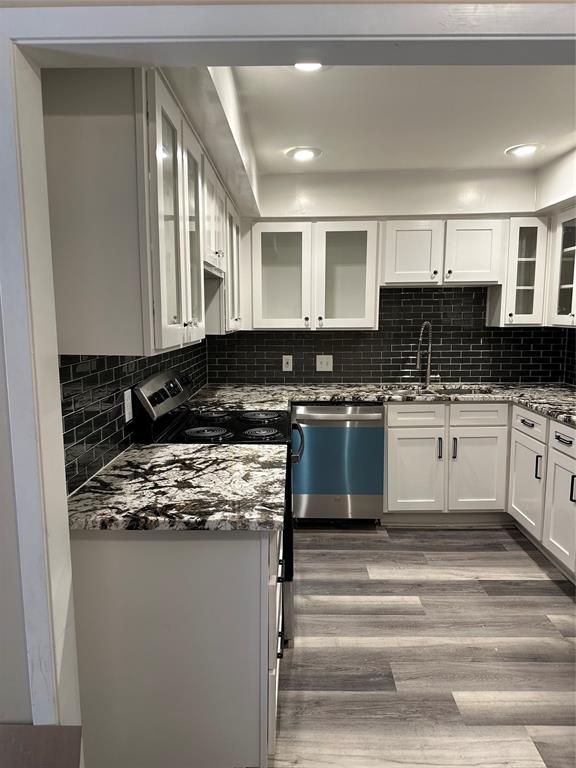 Planned Kitchen featuring white cabinetry, black subway tile backsplash, patterned stone countertops, and a black electric range with a stainless steel range hood.  These photos are of a different updated unit in the complex. The planned updates will be similar for this unit.