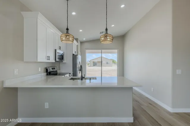 a kitchen with stainless steel appliances granite countertop a refrigerator a sink dishwasher a stove and white countertops with wooden floor