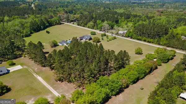 an aerial view of a residential houses with outdoor space and trees all around