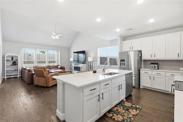 a large white kitchen with stainless steel appliances kitchen island granite countertop a refrigerator stove a sink dishwasher and white countertops with wooden floor