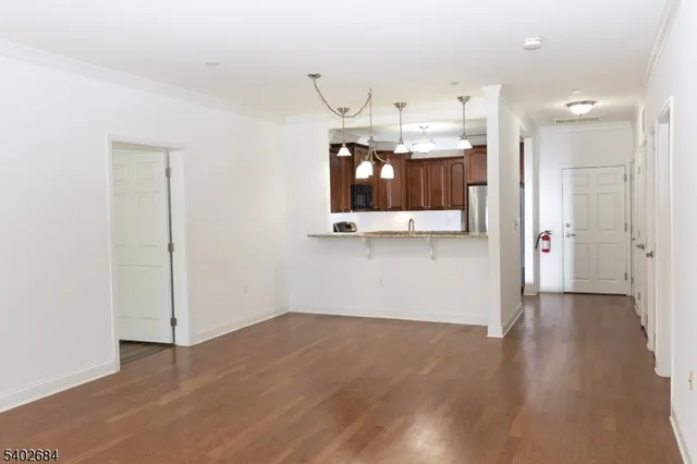an empty room with wooden floor and kitchen view