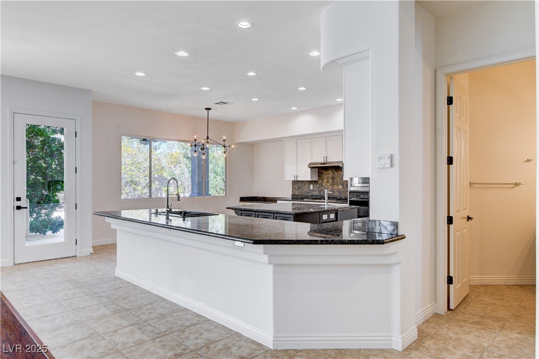 5148 Villa Vecchio Court Las Vegas, NV 89141 - Photo 23 of 71 Kitchen with dark stone counters, an island with sink, a sink, white cabinets, and tasteful backsplash