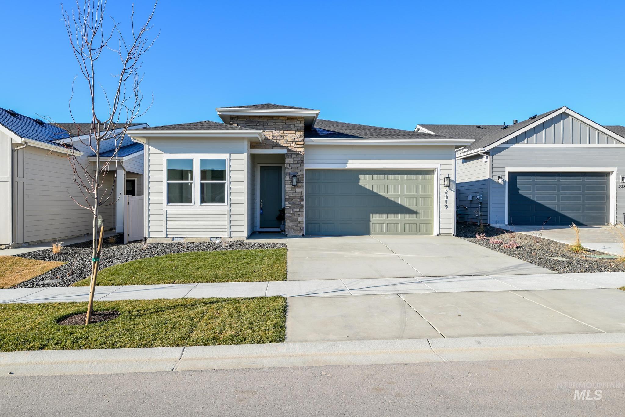 View of front of house featuring driveway, an attached garage, roof with shingles, and stone siding