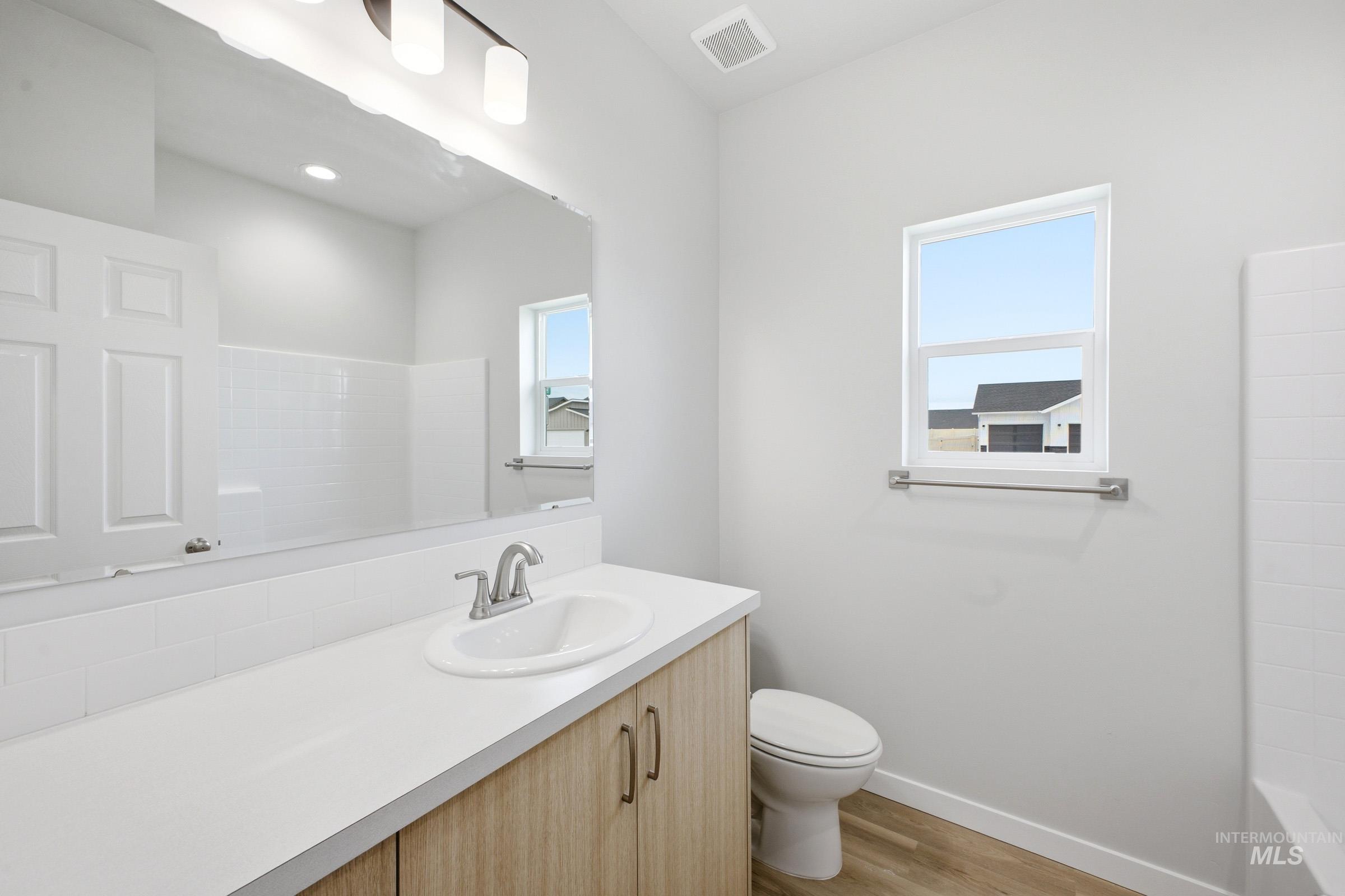 14104 Shiny Spruce Street Caldwell, ID 83607 - Photo 12 of 20 Bathroom vanity featuring a light wood-finish cabinet, white countertop, and an integrated sink with a brushed nickel faucet