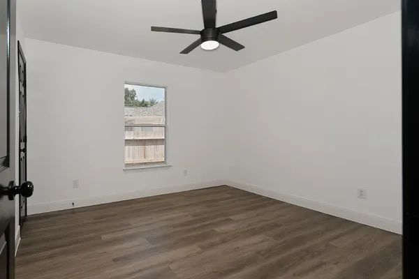an empty room with wooden floor fan and windows