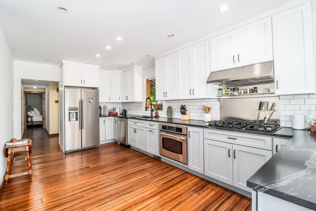 a kitchen with granite countertop a refrigerator oven a sink dishwasher and white cabinets with wooden floor