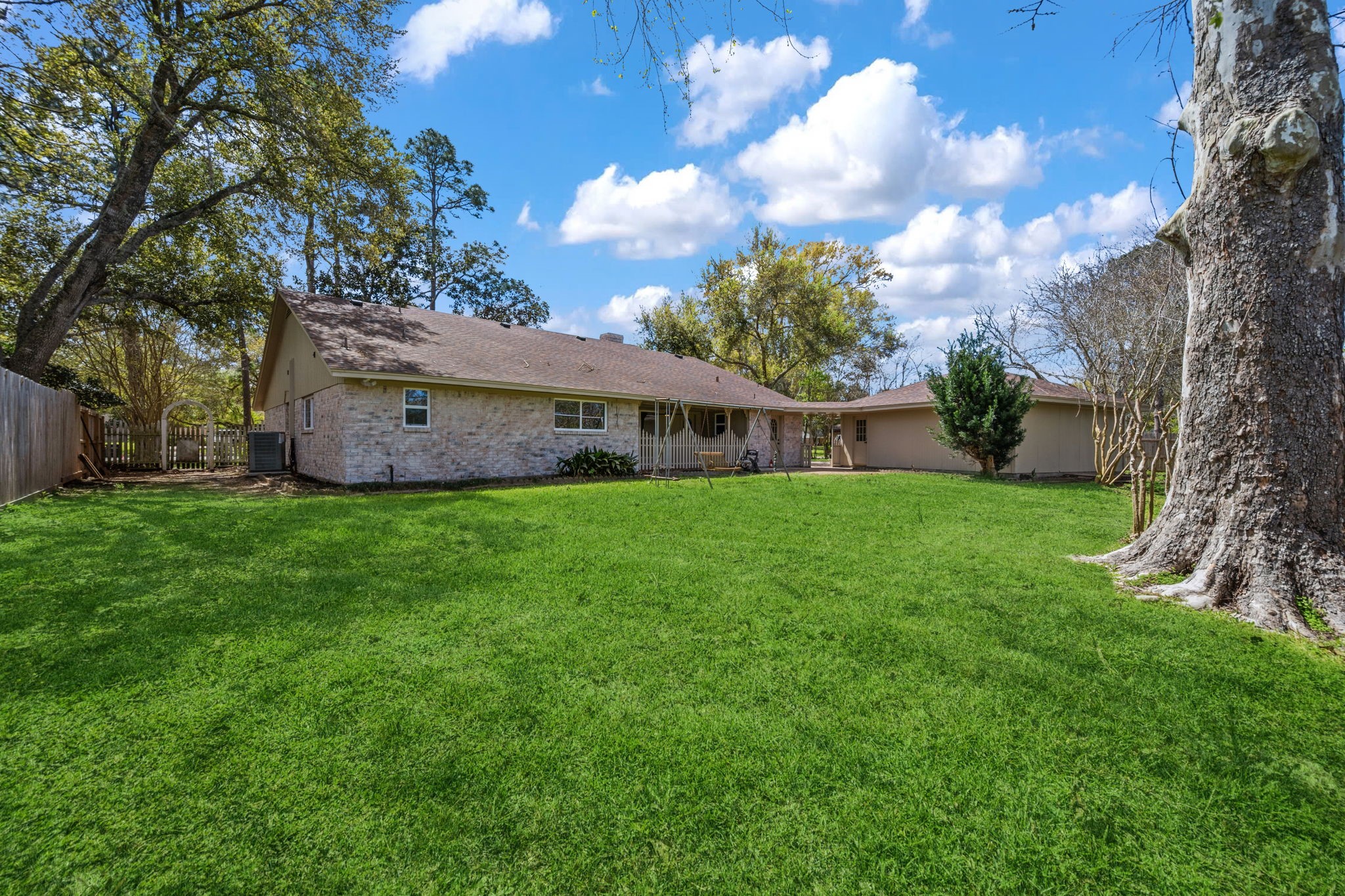 210 Ridgemont Drive Alvin, TX 77511 - Photo 25 of 27 This photo showcases a spacious backyard with lush green grass and mature trees, providing ample space for outdoor activities. The house features a cozy brick exterior and a detached structure, ideal for storage or a workshop. A wooden fence offers privacy, making it perfect for families or entertaining.