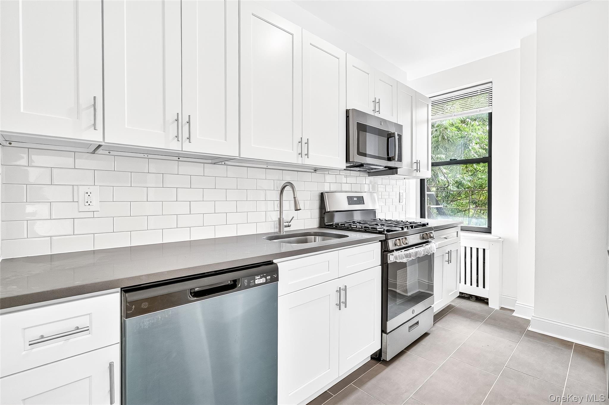 190 East Mosholu Parkway South, Unit 3C Bronx, NY 10458 - Photo 14 of 50 Kitchen featuring appliances with stainless steel finishes, white cabinetry, radiator, tasteful backsplash, and light tile patterned flooring