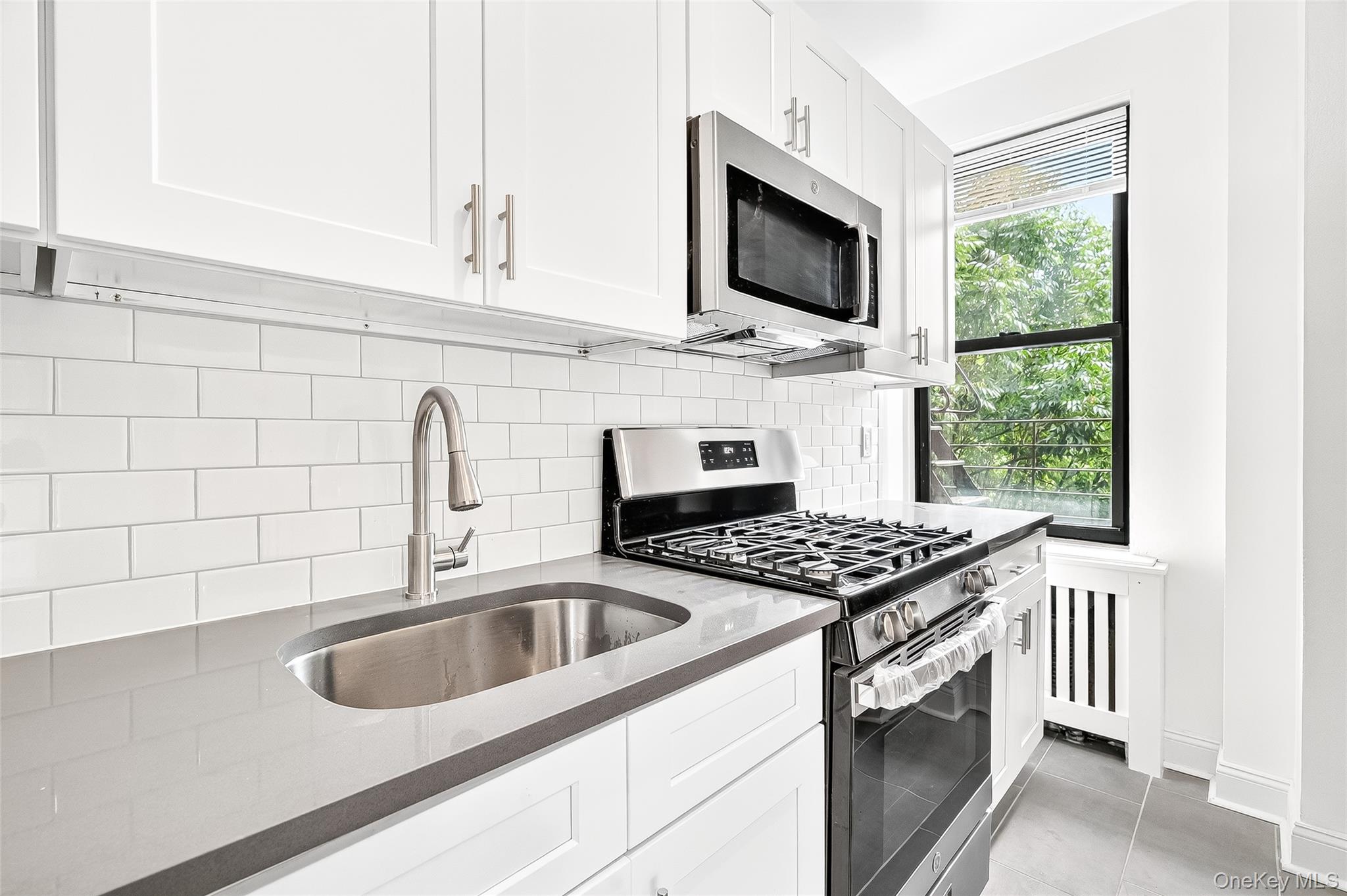 190 East Mosholu Parkway South, Unit 3C Bronx, NY 10458 - Photo 16 of 50 Kitchen featuring appliances with stainless steel finishes, dark stone counters, white cabinetry, decorative backsplash, and light tile patterned floors