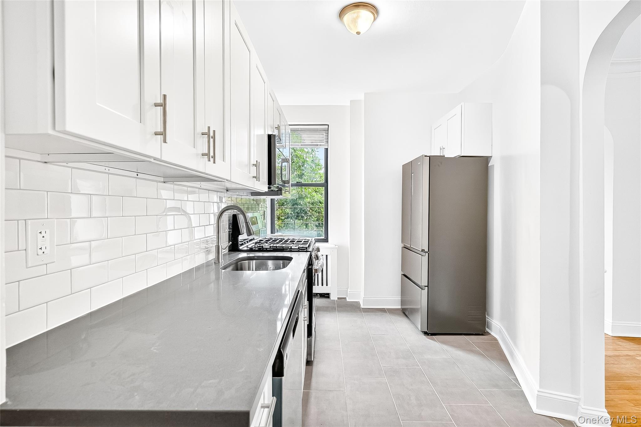 190 East Mosholu Parkway South, Unit 3C Bronx, NY 10458 - Photo 17 of 50 Kitchen with arched walkways, stainless steel appliances, light stone countertops, white cabinetry, and decorative backsplash