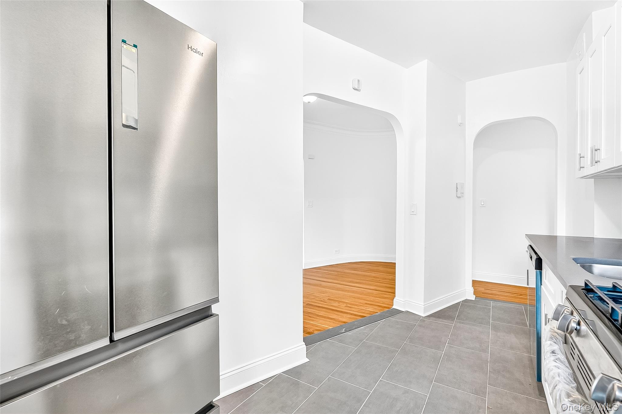 190 East Mosholu Parkway South, Unit 3C Bronx, NY 10458 - Photo 19 of 50 Kitchen featuring stainless steel appliances, white cabinetry, arched walkways, dark tile patterned flooring, and dark stone counters