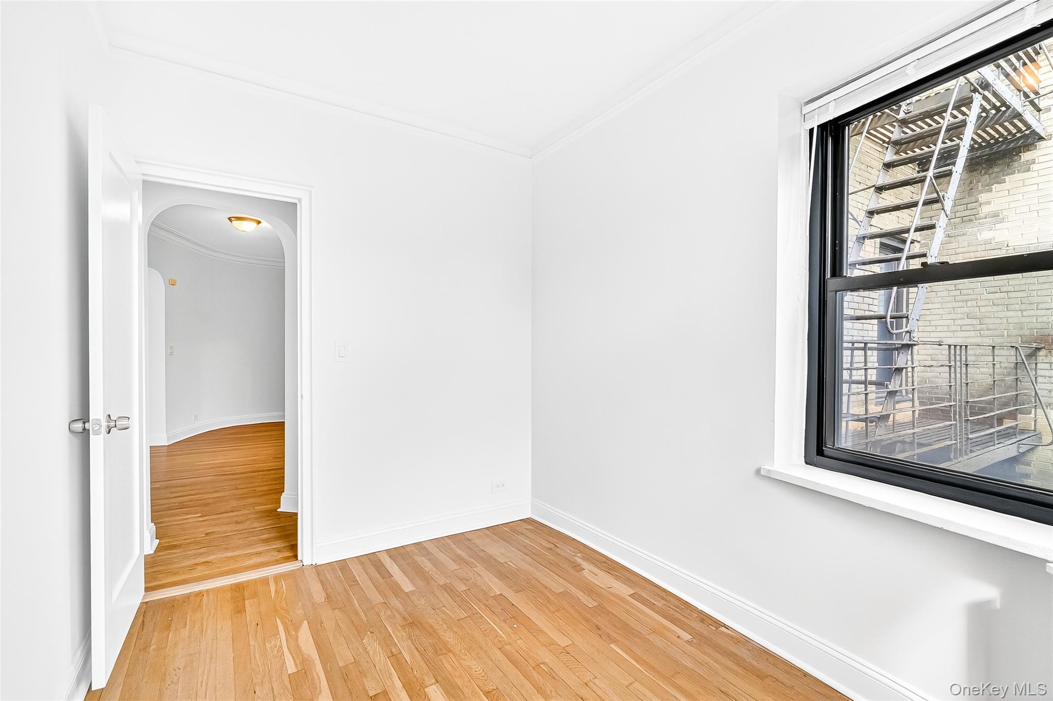 190 East Mosholu Parkway South, Unit 3C Bronx, NY 10458 - Photo 31 of 50 Empty room with crown molding, light wood-style flooring, and arched walkways