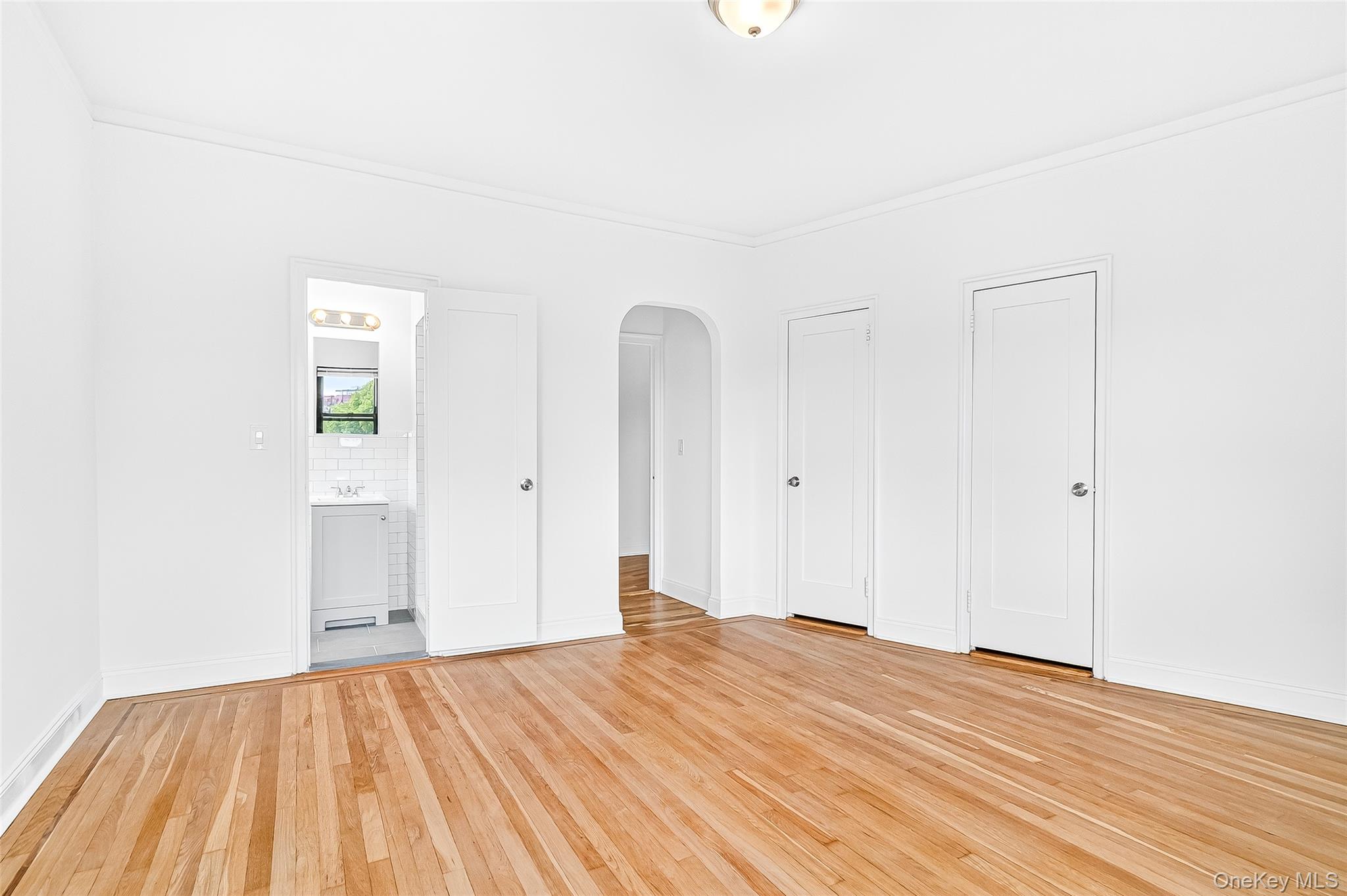 190 East Mosholu Parkway South, Unit 3C Bronx, NY 10458 - Photo 36 of 50 Unfurnished bedroom featuring two closets, light wood-type flooring, arched walkways, ornamental molding, and connected bathroom