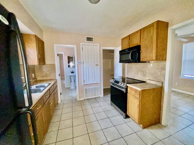 6100 Felix Avenue, Unit B Austin, TX 78741 - Photo 5 of 9 Kitchen featuring wood finish cabinetry, black appliances, light countertops, and light tile patterned floors
