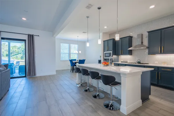 a kitchen with kitchen island stainless steel appliances a dining table chairs sink and white cabinets