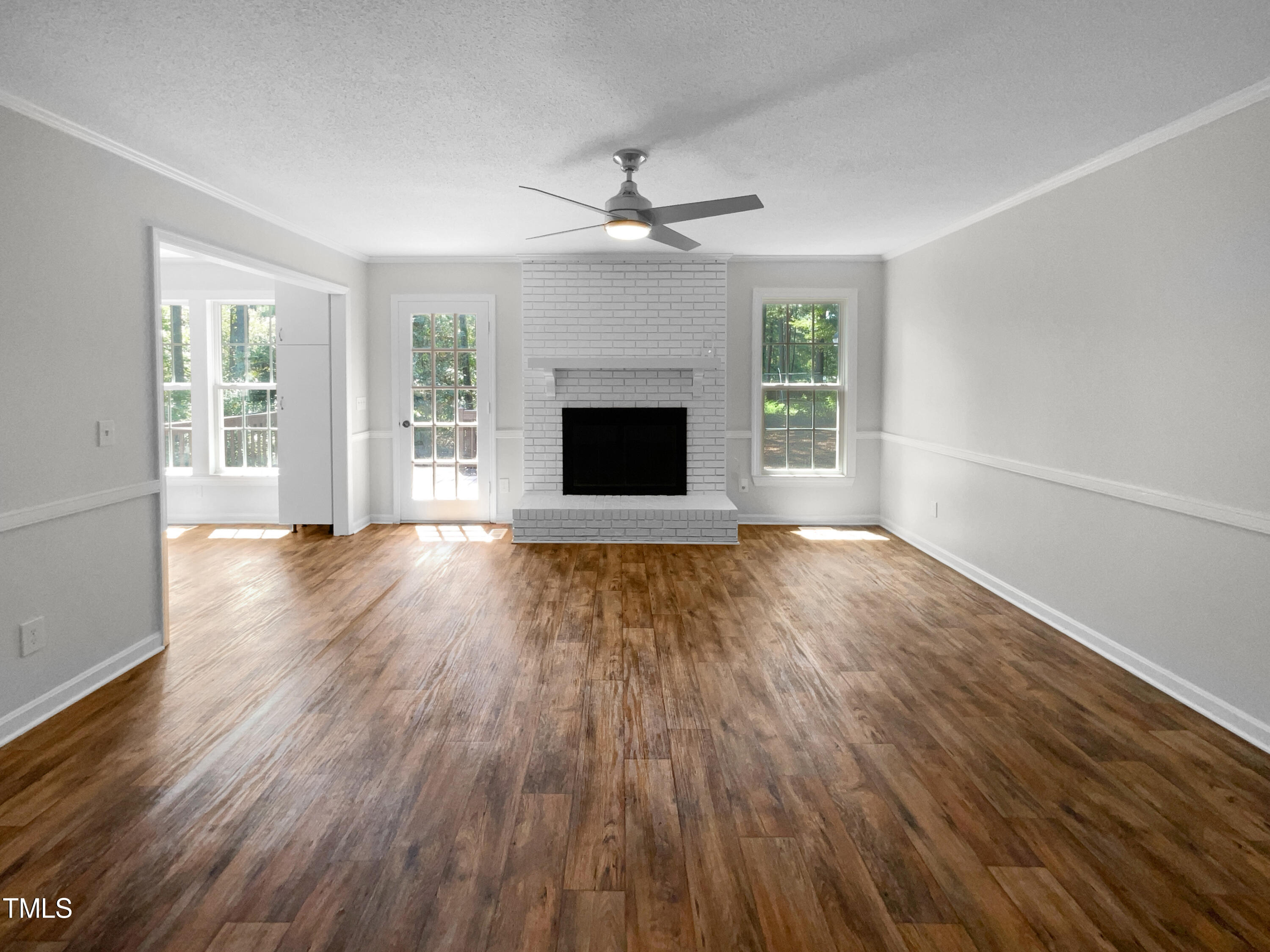 1516 Clayton Road Fuquay-Varina, NC 27526 - Photo 3 of 17 an empty room with wooden floor a ceiling fan a fireplace and windows