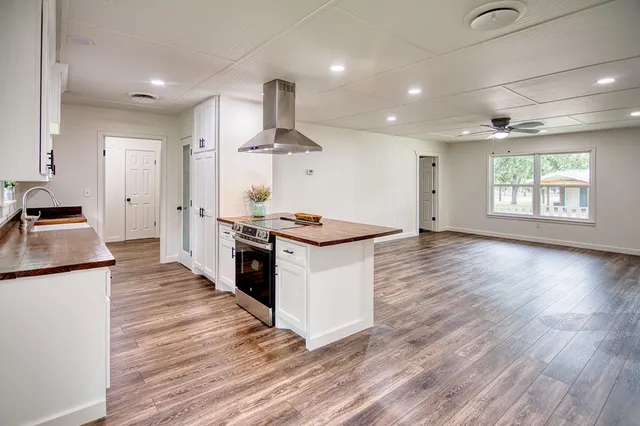 an empty room with wooden floor chandelier fan and windows