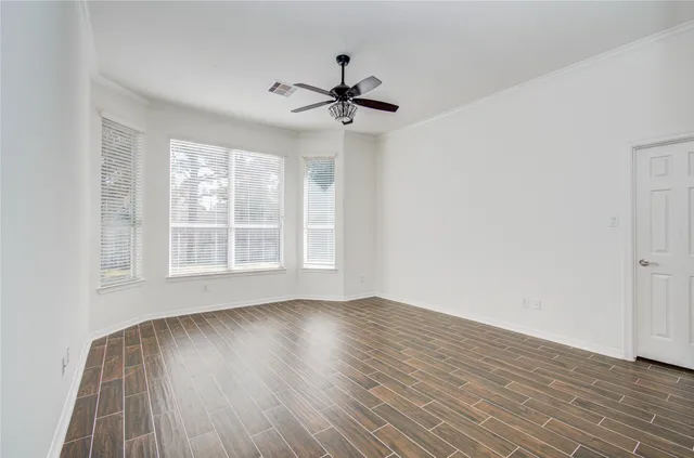 an empty room with wooden floor a ceiling fan and windows