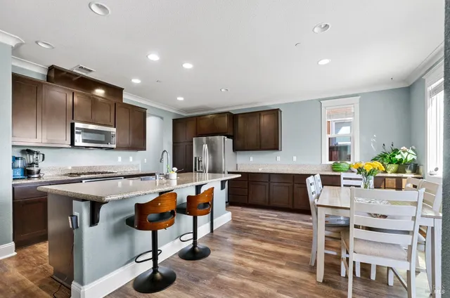 a kitchen with stainless steel appliances granite countertop a stove top oven a sink dishwasher a dining table and chairs with wooden floor