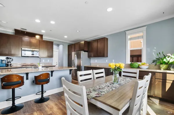 a kitchen with stainless steel appliances kitchen island granite countertop a stove a refrigerator a kitchen island a stove a dining table and chairs with wooden floor