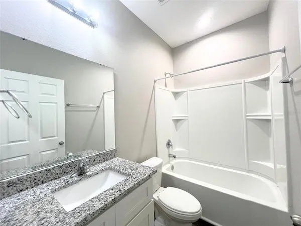 a bathroom with a granite countertop bathtub shower sink vanity mirror and toilet