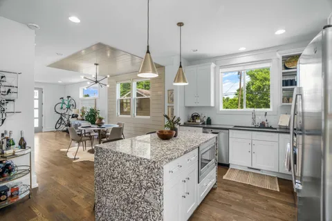 a kitchen with stainless steel appliances granite countertop a stove a sink dishwasher a refrigerator and white cabinets next to a window