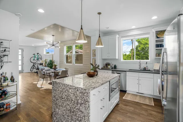 a kitchen with stainless steel appliances granite countertop a stove a sink dishwasher a refrigerator and white cabinets next to a window