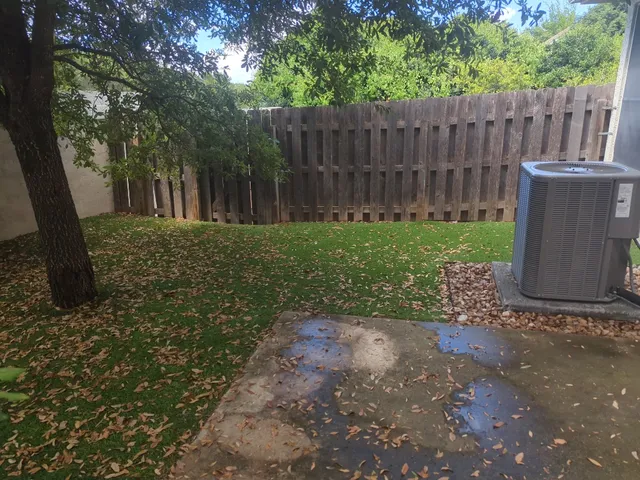 a view of a backyard with wooden fence and large trees