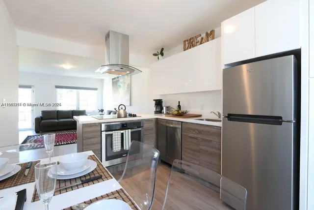 a kitchen with a refrigerator a sink dishwasher a dining table and chairs with wooden floor