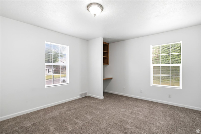 1341 29th Street Ogden, UT 84403 - Photo 19 of 37 Bright interior room with plush carpeting, two windows, and a built-in wooden desk with shelving