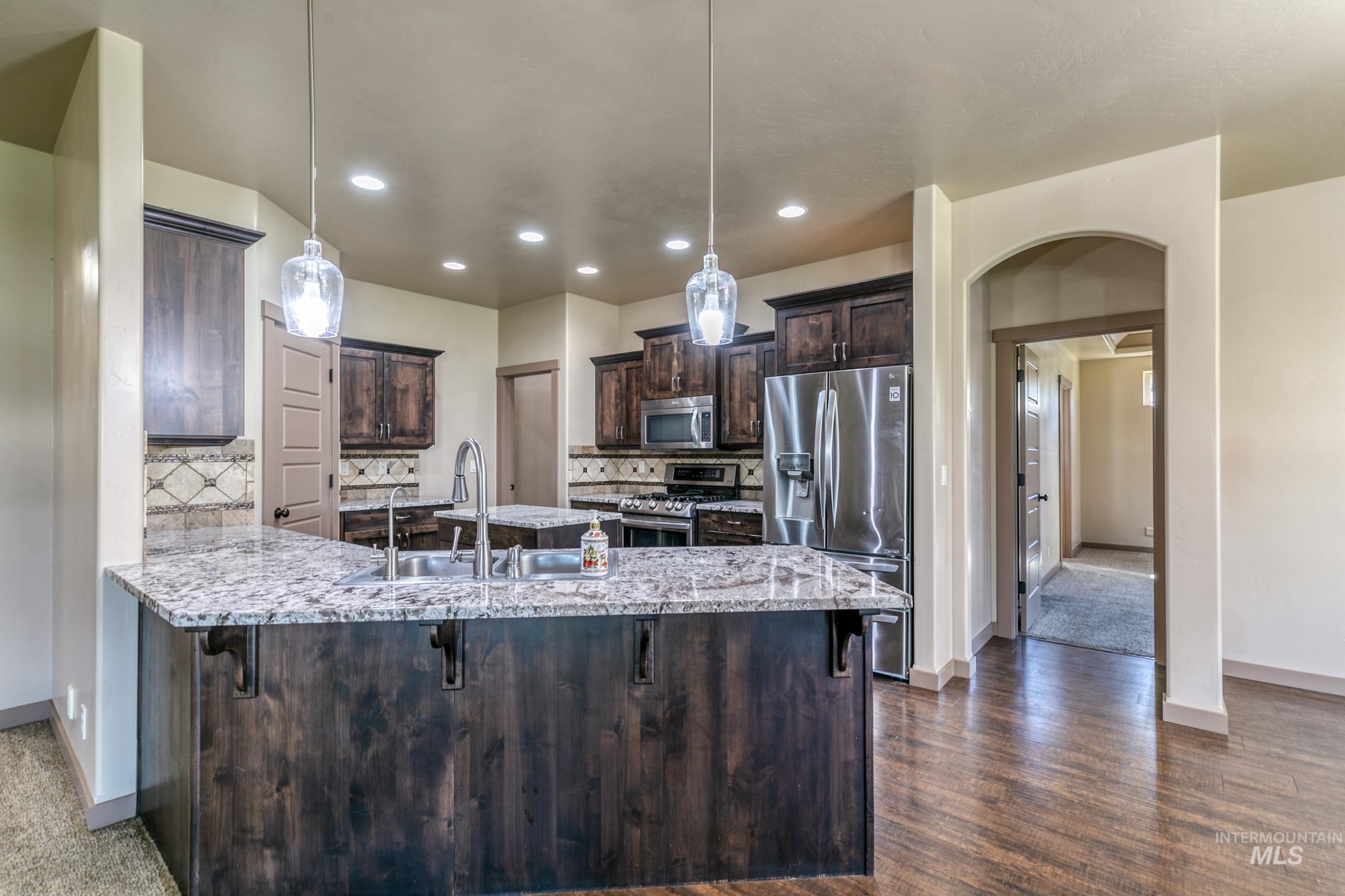 4316 Middlesboro Way Caldwell, ID 83607 - Photo 10 of 33 Kitchen featuring wood-finish flooring, dark wood cabinetry, light-toned countertops, and a tile backsplash