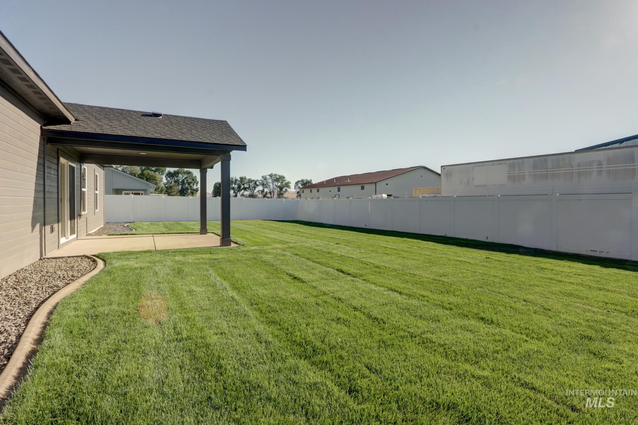 848 North 5th Street Nyssa, OR 97913 - Photo 40 of 49 Expansive lawn area featuring a covered patio with concrete flooring, a white privacy fence, and a gravel border with concrete curbing