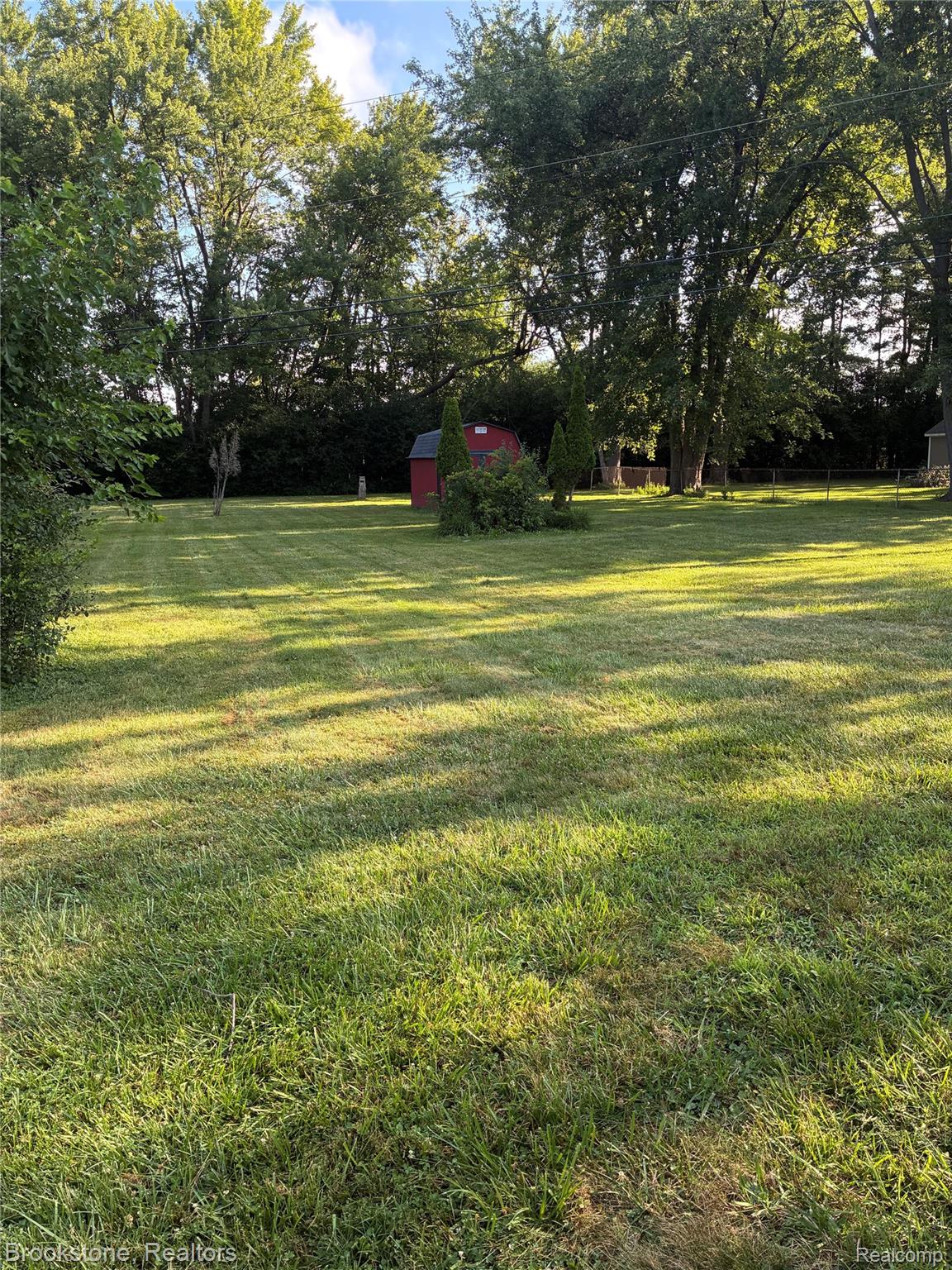 Expansive grassy yard with mature trees and a red storage shed