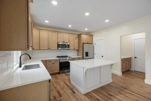 a kitchen with stainless steel appliances granite countertop a sink a stove a refrigerator cabinets and a wooden floor