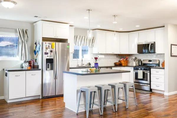 a kitchen with stainless steel appliances granite countertop a stove top oven a sink a refrigerator and white cabinets with wooden floor