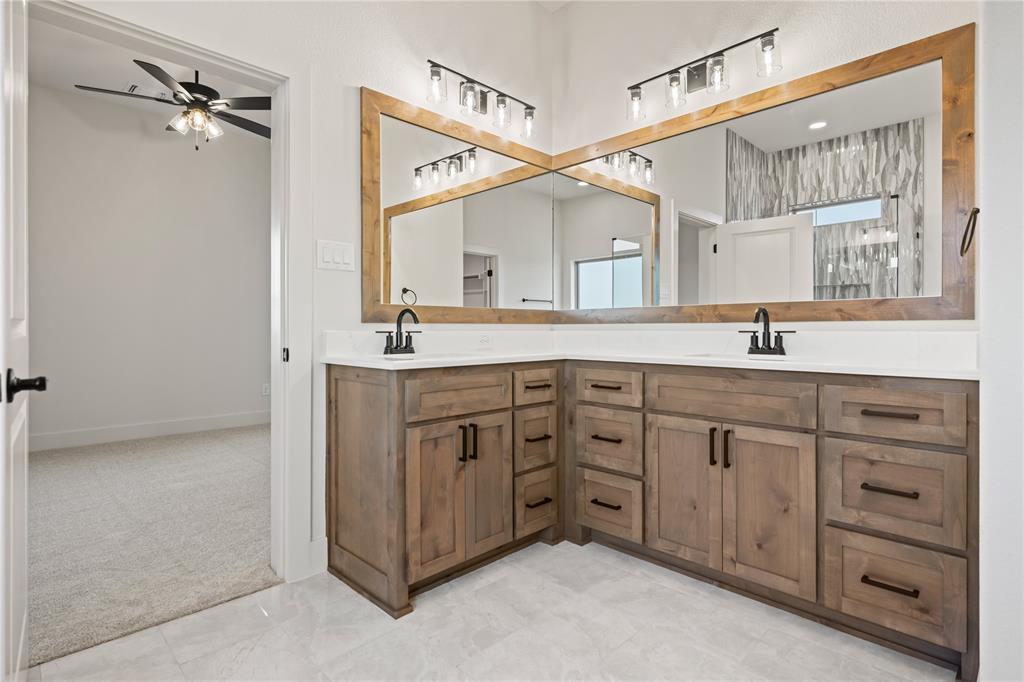 7004 Rnch Vw Place Springtown, TX 76082 - Photo 13 of 25 Dual wood-frame mirrors above a corner vanity with wood-finish cabinetry, white countertops, and matte black fixtures