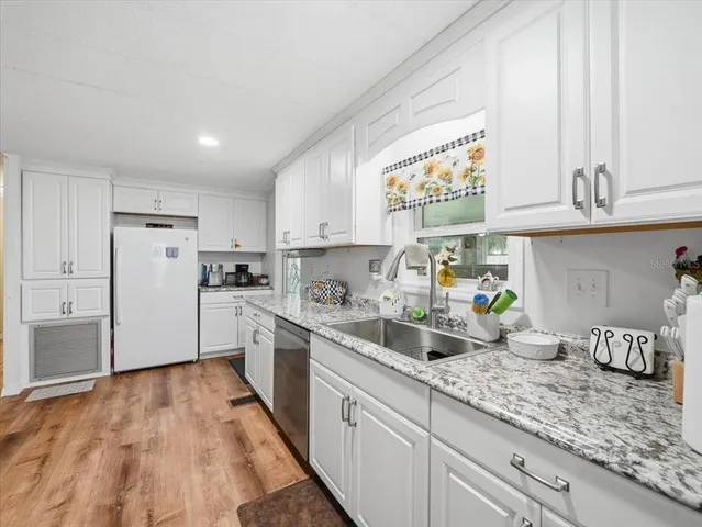 a kitchen with granite countertop a sink stainless steel appliances white cabinets and a window