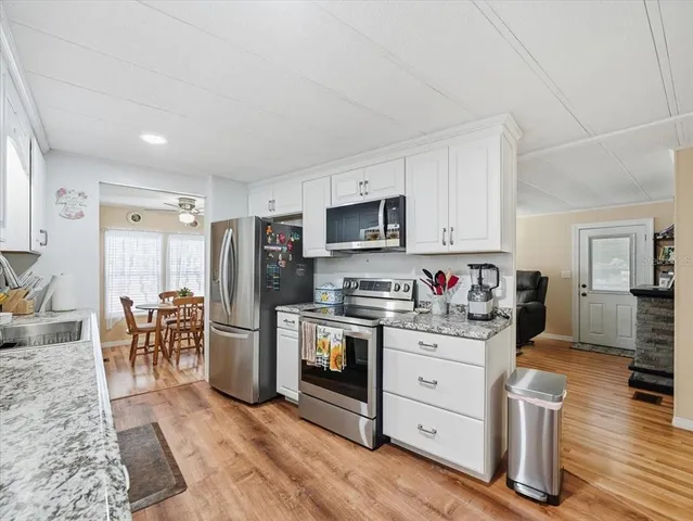 a kitchen with stainless steel appliances a stove a sink dishwasher a refrigerator cabinets and a dining table with wooden floor