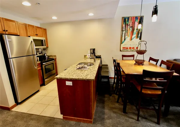 a kitchen with stainless steel appliances granite countertop a refrigerator a sink a stove a dining table and chairs