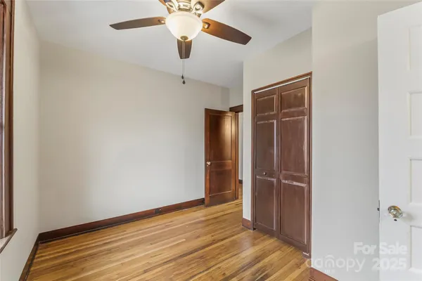 an empty room with wooden floor closet and windows