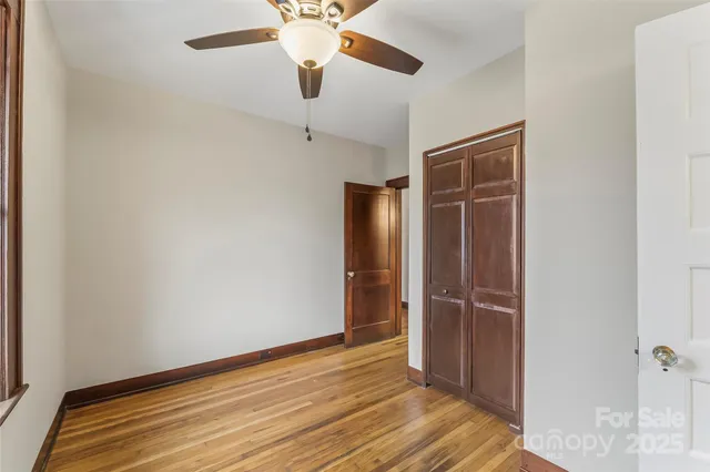 an empty room with wooden floor closet and windows