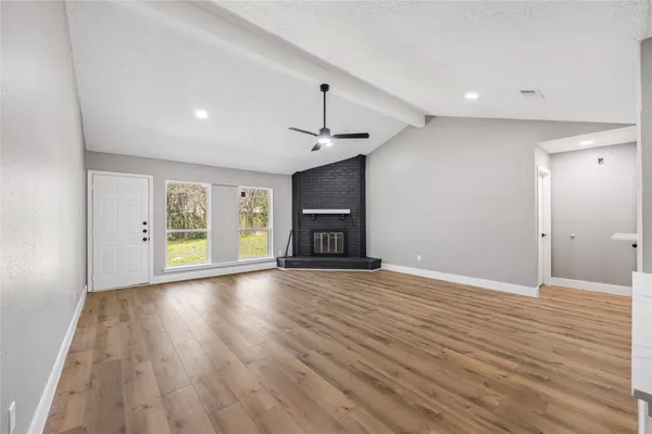 a view of an empty room with wooden floor fireplace and a window