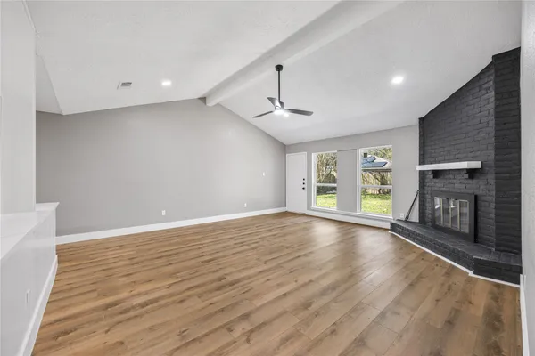 an empty room with wooden floor fireplace and windows