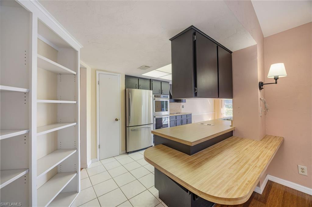 379 Torrey Pines Point Naples, FL 34113 - Photo 10 of 21 Built-in white shelving, wood-finish countertops, black cabinetry, white tile flooring, and stainless steel refrigerator